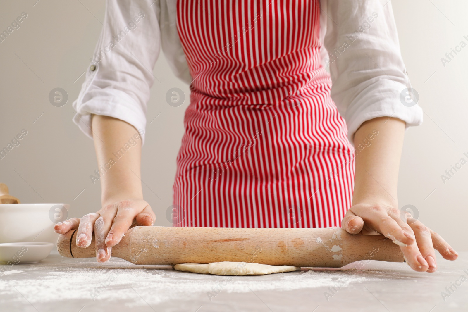 Photo of Woman rolling fresh dough at light grey table, closeup. Cooking grissini