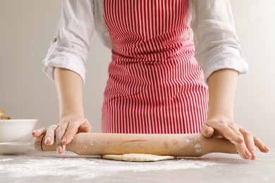 Photo of Woman rolling fresh dough at light grey table, closeup. Cooking grissini