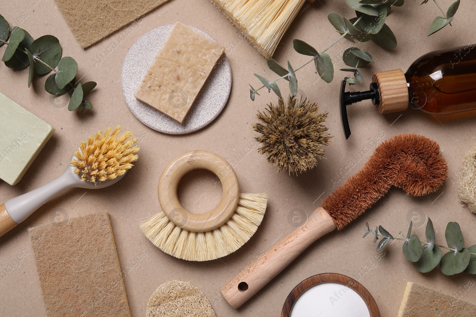 Photo of Cleaning brushes, baking soda, soap, sponges and eucalyptus leaves on pale brown background, flat lay