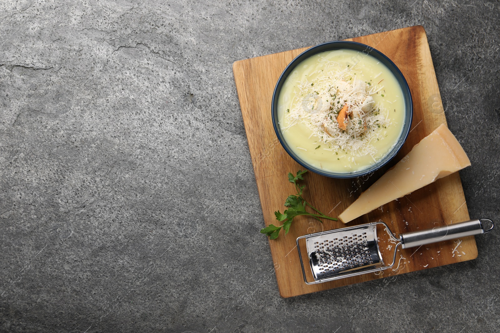 Photo of Delicious cream soup with parmesan cheese and croutons in bowl on grey table, top view. Space for text