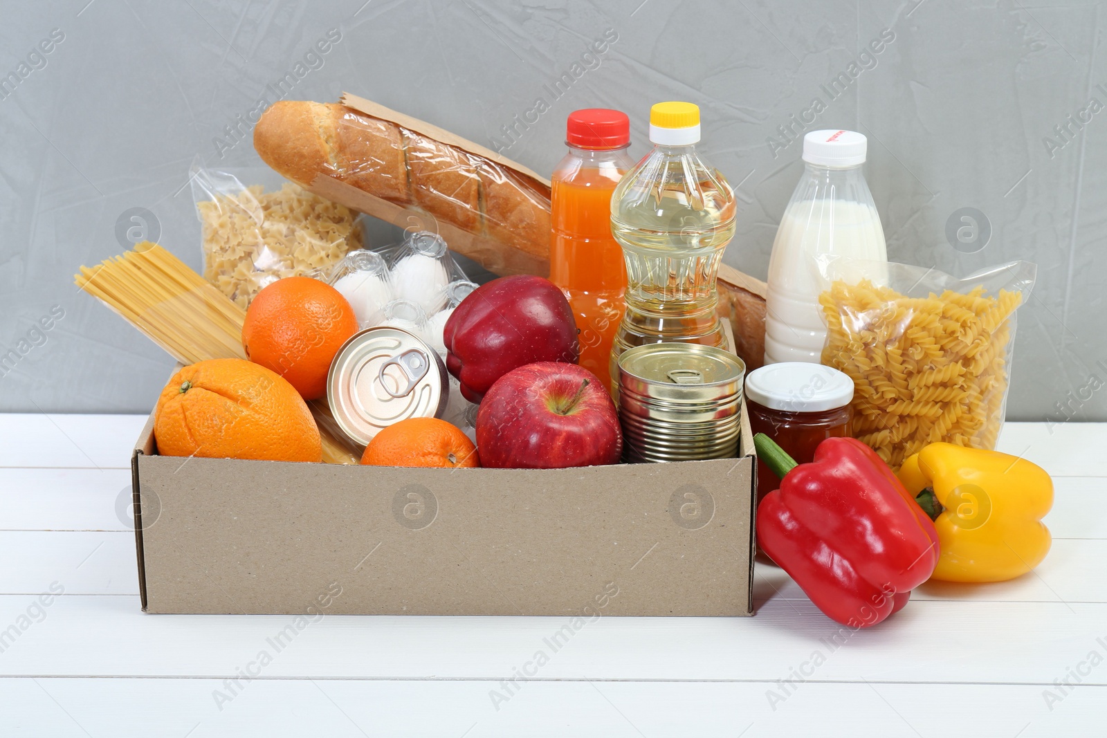 Photo of Humanitarian aid. Different food products for donation in box on white wooden table