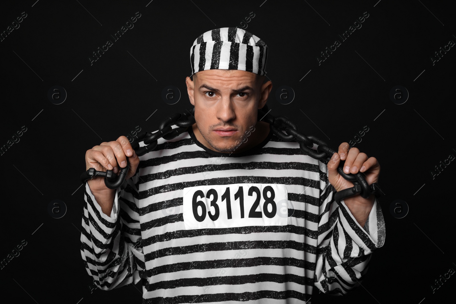 Photo of Prisoner in striped uniform with chained hands on black background