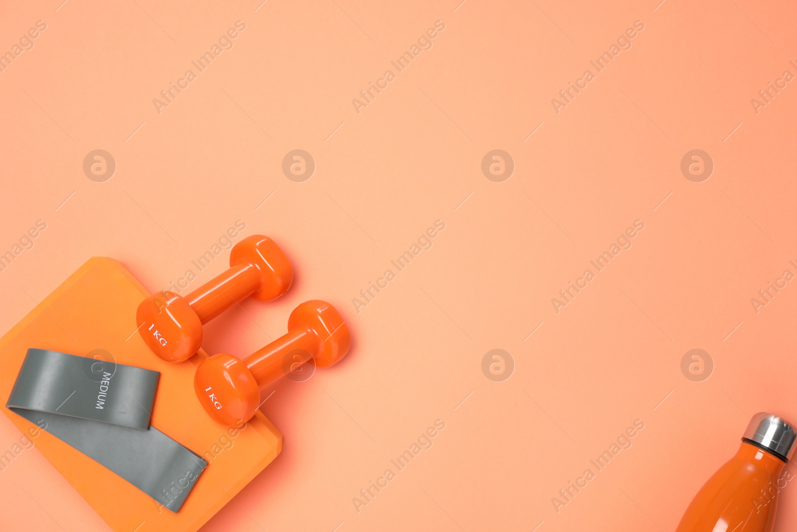 Photo of Dumbbells, thermo bottle, fitness elastic band and yoga block on coral background, flat lay. Space for text