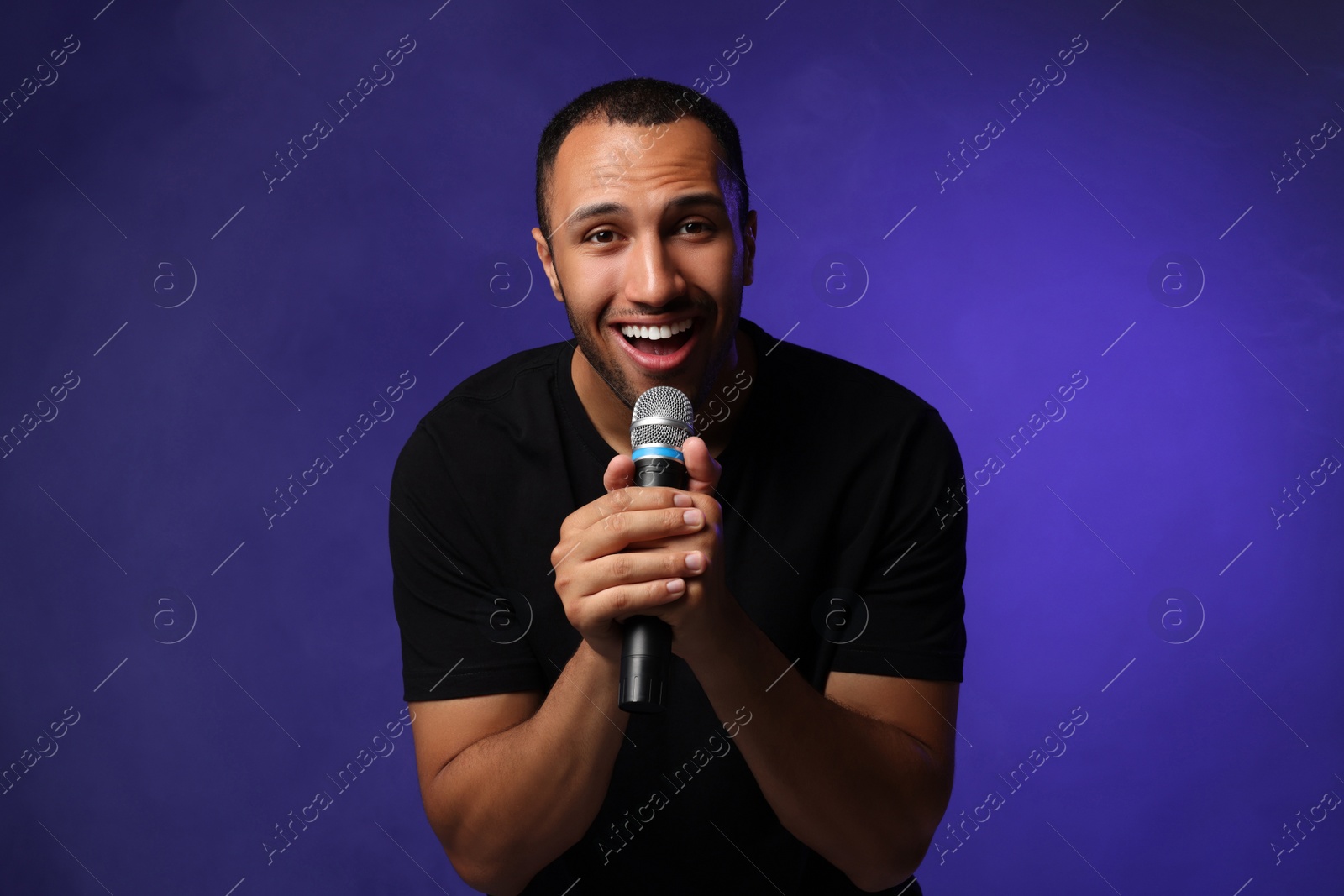 Photo of Handsome man with microphone singing on blue background