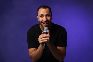 Handsome man with microphone singing on blue background