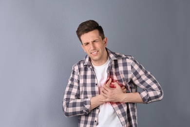 Young man having heart attack on color background