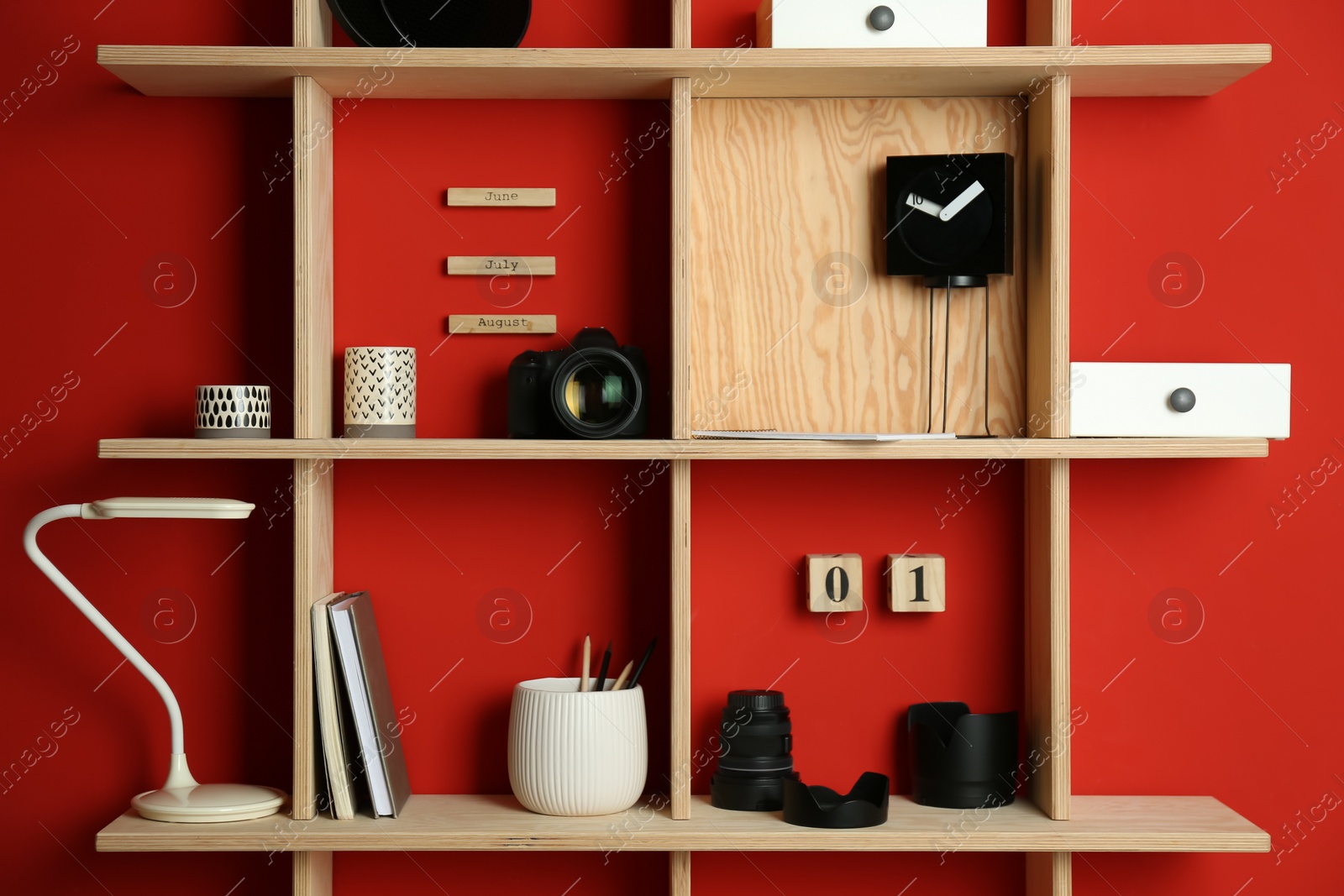 Photo of Stylish wooden shelves with photography equipment and decorative elements on red wall