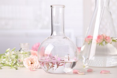 Photo of Flask with rosebay flowers on white wooden table. Essential oil extraction