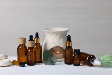 Different aromatherapy products, burning candle and eucalyptus leaves on white wooden table against light background