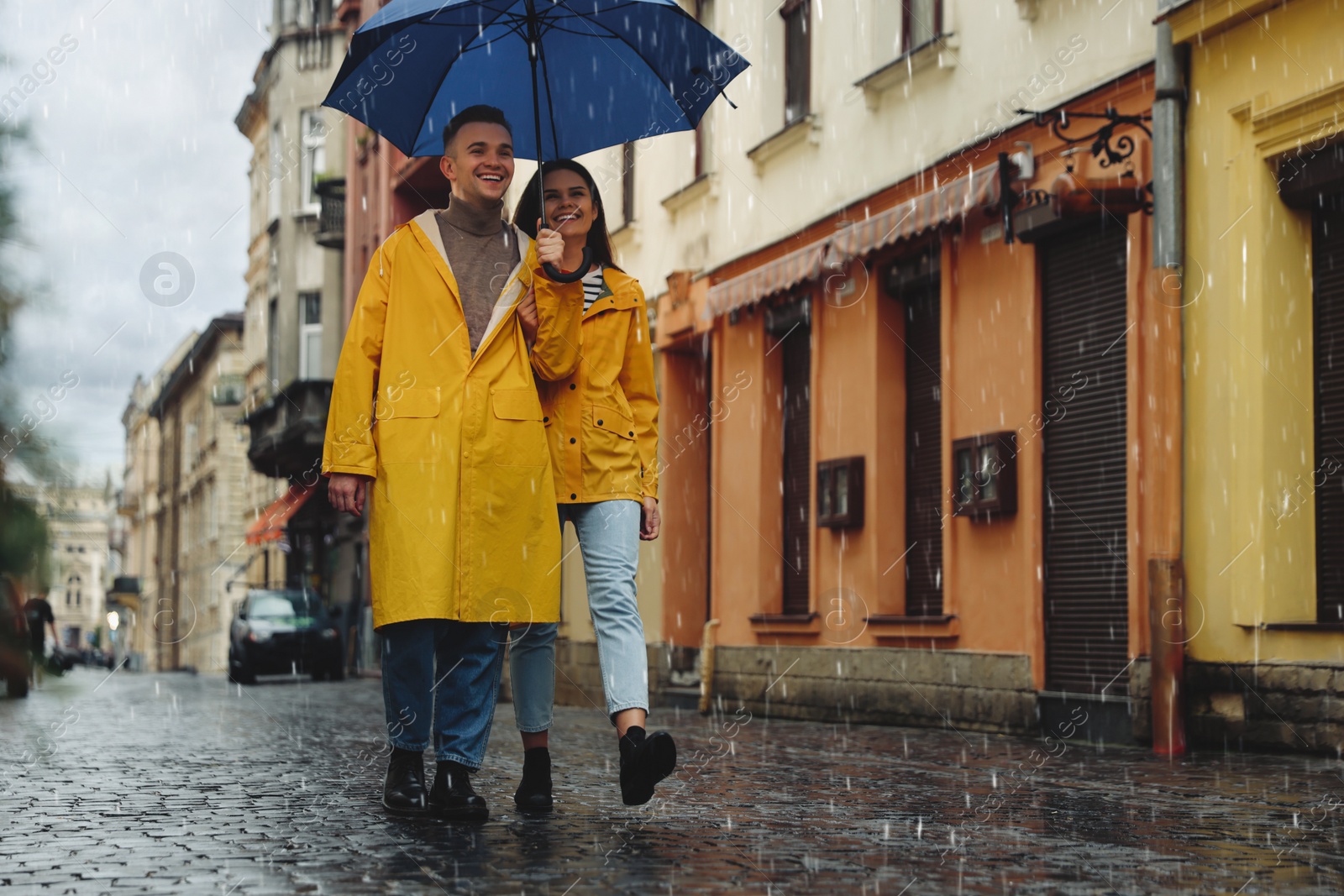 Photo of Lovely young couple with umbrella walking under rain on city street