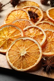Photo of Many dry orange slices and spices on black table, closeup