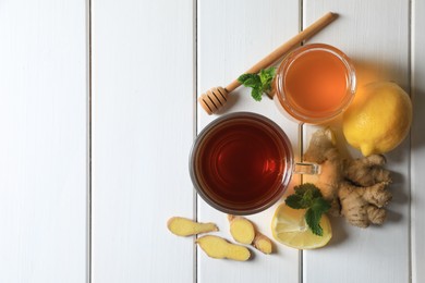 Cup of delicious ginger tea, honey and lemons on white wooden table, flat lay. Space for text