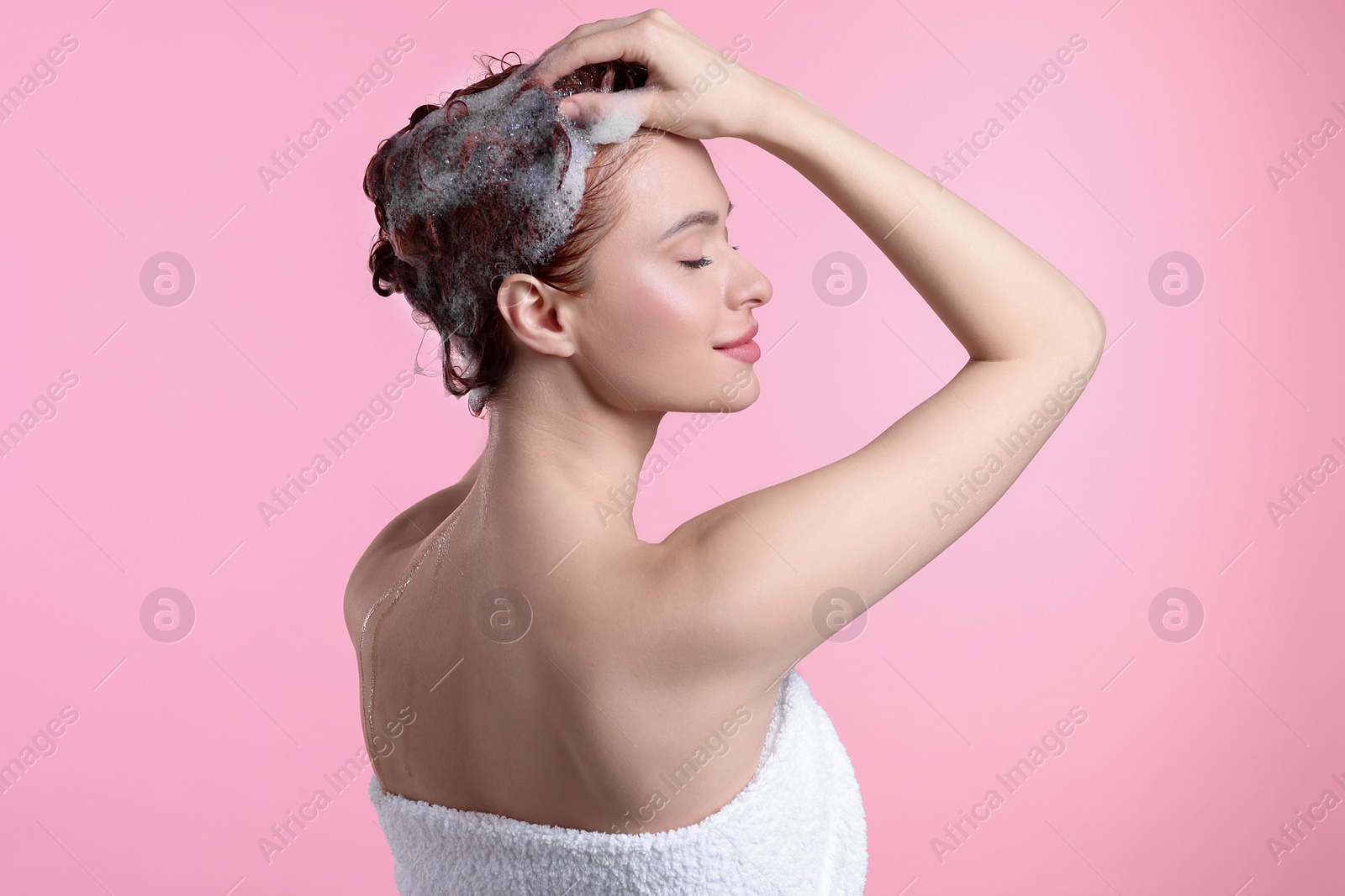 Photo of Happy young woman washing her hair with shampoo on pink background