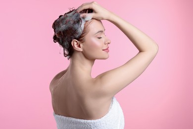 Happy young woman washing her hair with shampoo on pink background