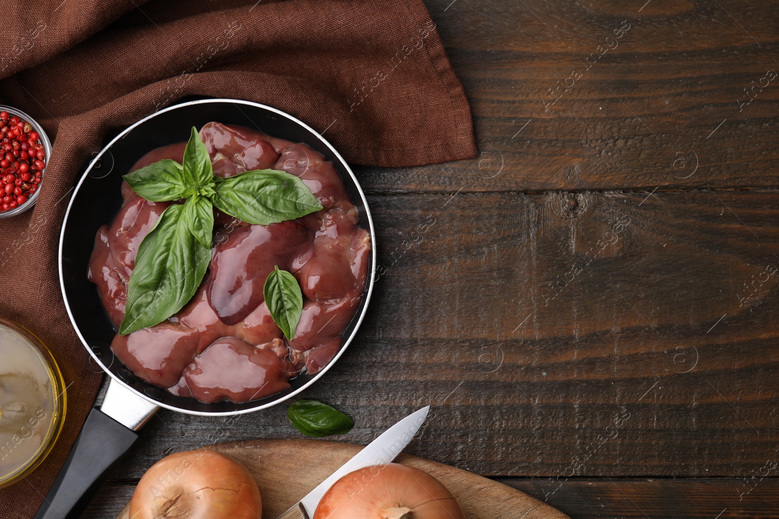 Photo of Raw chicken liver with basil in frying pan and products on wooden table, flat lay. Space for text
