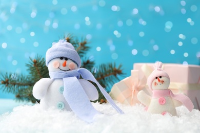 Cute toy snowmen on snow against blurred background