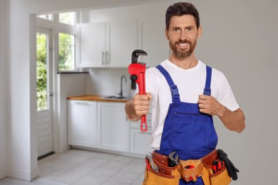 Plumber with pipe wrench and tool belt in kitchen, space for text