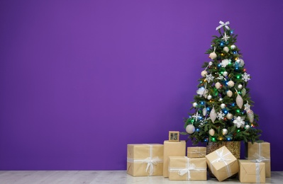 Beautiful Christmas tree and gift boxes near purple wall indoors, space for text