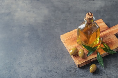 Wooden board with olives and fresh oil on grey background