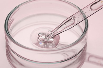 Glass pipette and petri dish with liquid on pink background, closeup