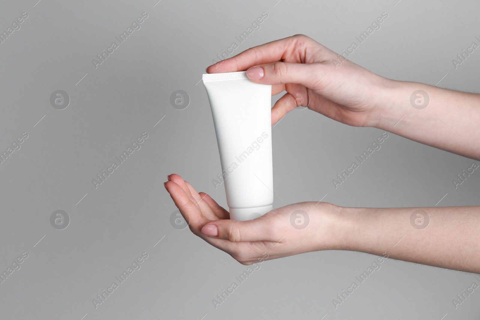 Photo of Woman holding tube of cream on grey background, closeup. Space for text