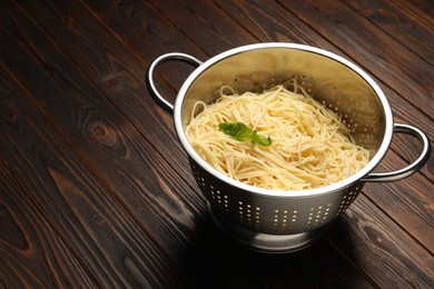 Photo of Cooked pasta in metal colander on wooden table, closeup. Space for text