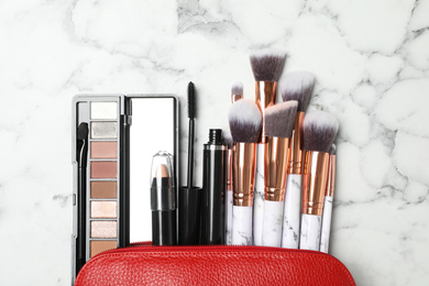 Photo of Cosmetic bag with makeup products and beauty accessories on white marble background, flat lay