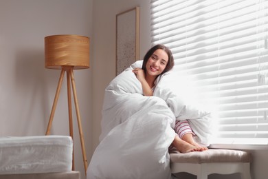 Photo of Beautiful young woman wrapped with soft blanket near window at home