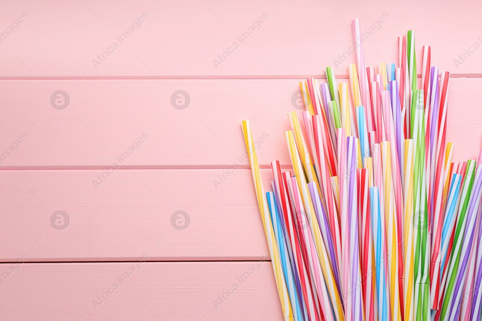 Photo of Colorful plastic drinking straws on pink wooden table, flat lay. Space for text