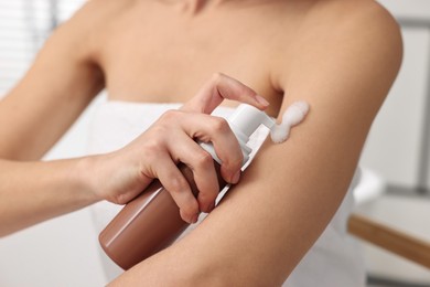 Photo of Woman applying self-tanning product onto arm indoors, closeup