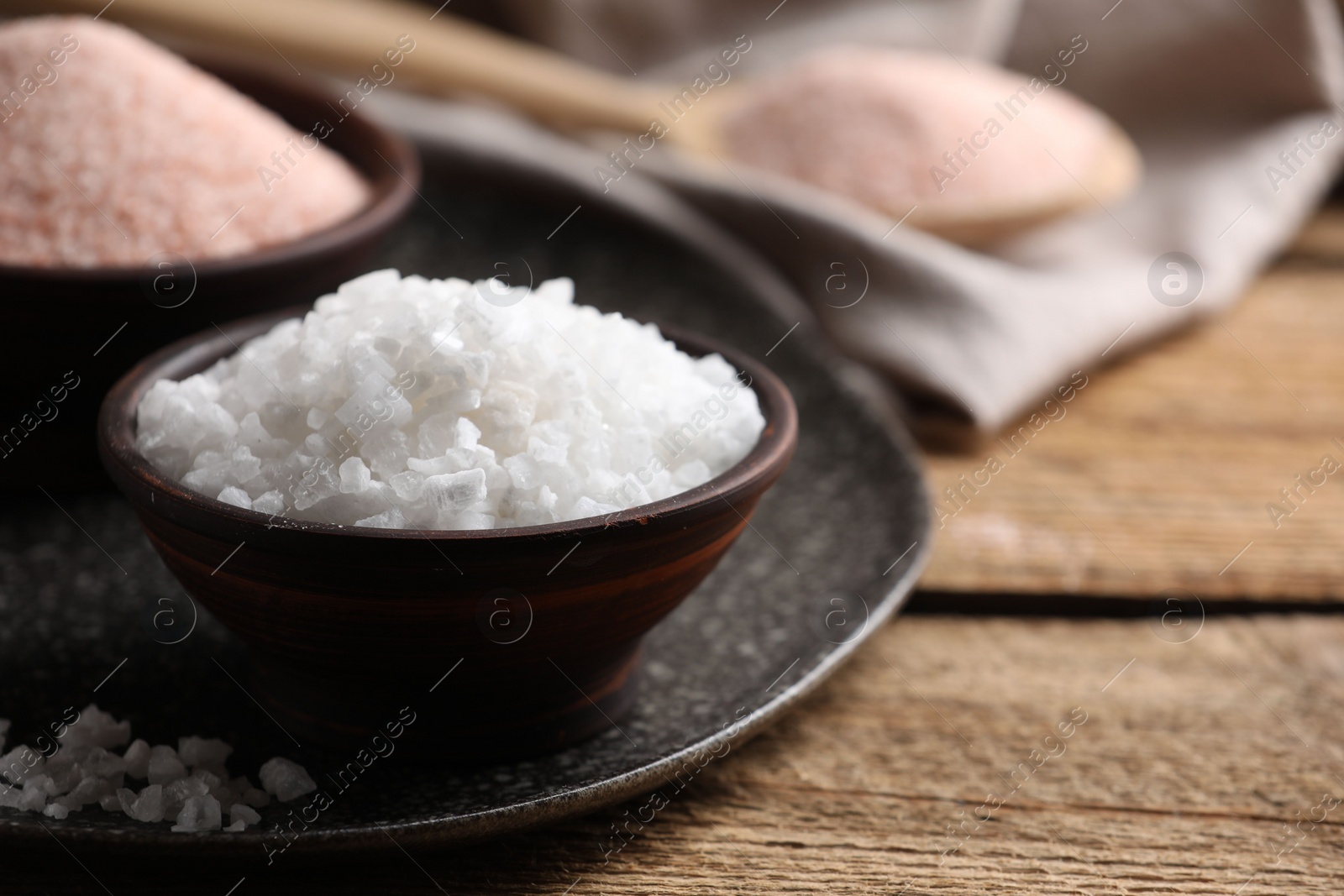 Photo of Different salt in bowls on wooden table, closeup. Space for text