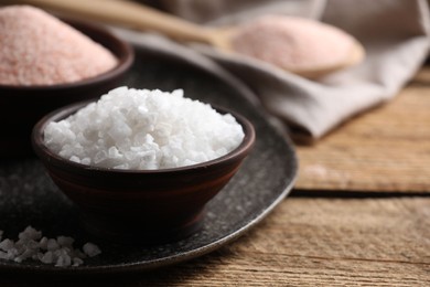 Photo of Different salt in bowls on wooden table, closeup. Space for text