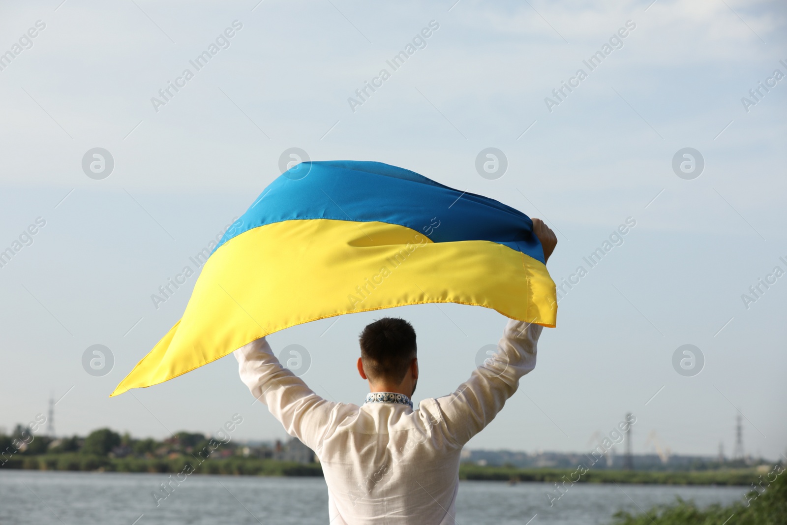 Photo of Man in vyshyvanka with flag of Ukraine outdoors, back view