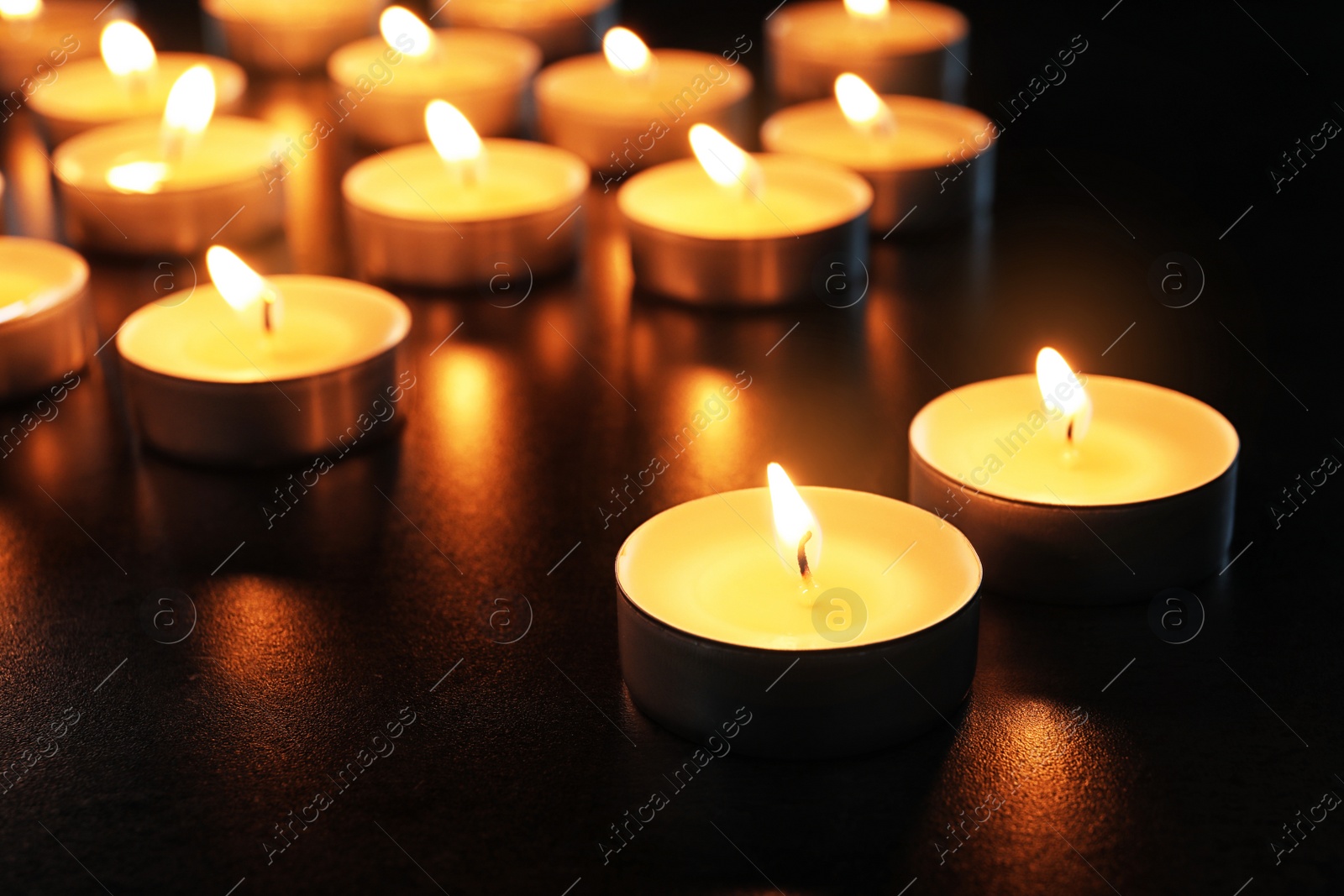 Photo of Wax candles burning on table in darkness, closeup