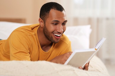 Photo of Happy African American man reading book on bed at home