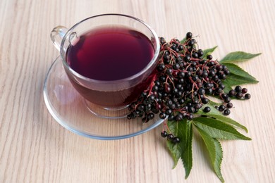 Glass cup of tasty elderberry tea and Sambucus berries on wooden table