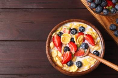 Photo of Bowl of tasty crispy corn flakes with milk and berries on wooden table, flat lay. Space for text