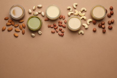 Different types of delicious nut butters and ingredients on brown background, flat lay. Space for text