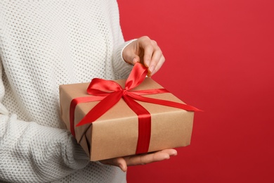 Photo of Woman holding Christmas gift box on red background, closeup