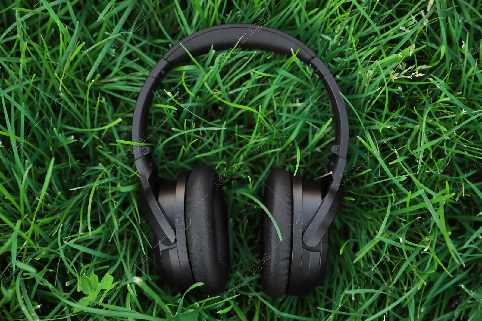 Photo of Black wireless headphones on green grass outdoors, top view