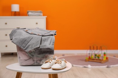 Laundry basket with baby clothes and shoes on white wooden table in child room, space for text