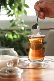 Photo of Woman adding sugar into aromatic tea at wooden table indoors, closeup