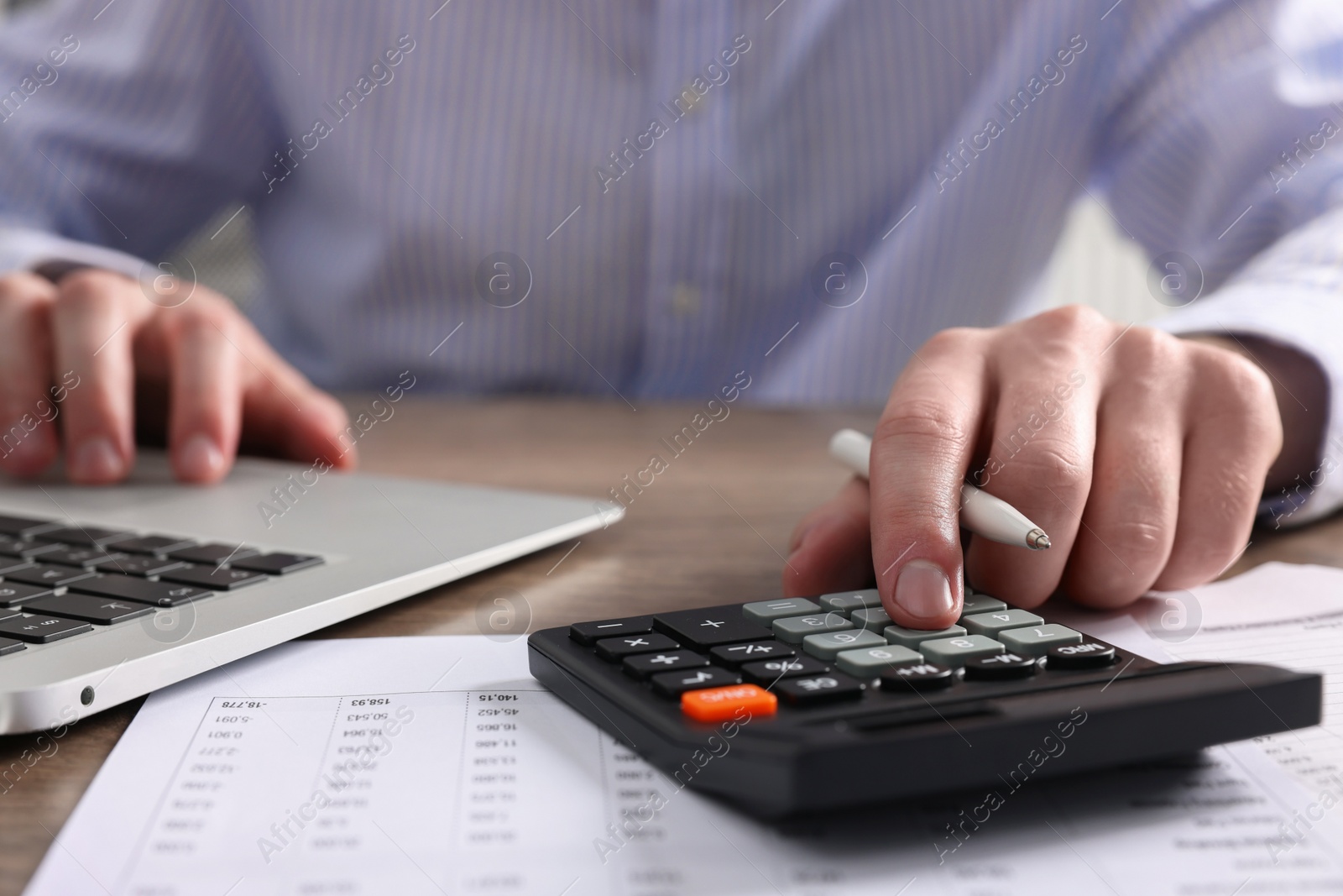 Photo of Man using calculator while working on laptop at table, closeup