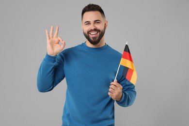 Photo of Young man with flag of Germany showing ok gesture on light grey background