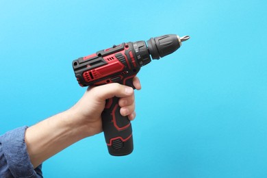 Handyman holding electric screwdriver on light blue background, closeup