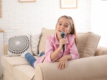 Photo of Cute girl with microphone on sofa in living room