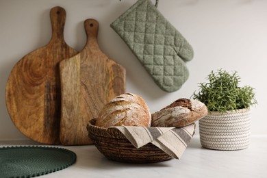 Wicker bread basket with freshly baked loaves on white marble table in kitchen