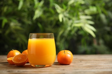 Glass of fresh tangerine juice and fruits on wooden table. Space for text