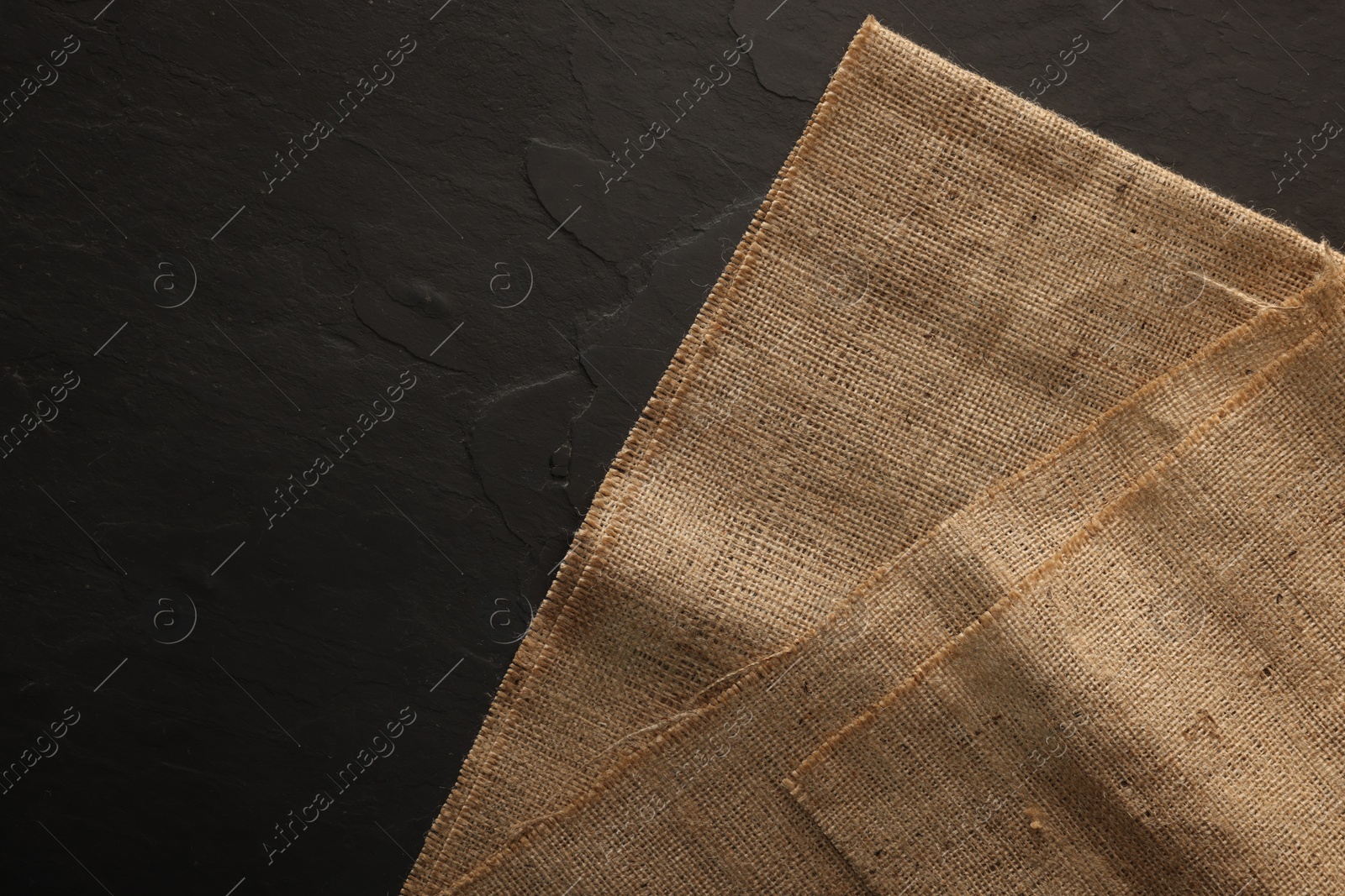 Photo of Natural burlap fabric on black table, top view. Space for text