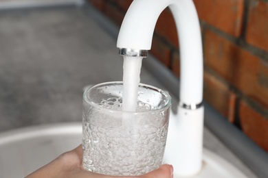 Woman filling glass with water from faucet in kitchen, closeup